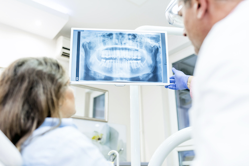 Photo of health dental professional in blue scrubs examining dental x-ray on computer screen, isolated dentist office. People, medicine, stomatology, technology and health care concept - dentists looking to x-ray scan on monitor at dental clinic.